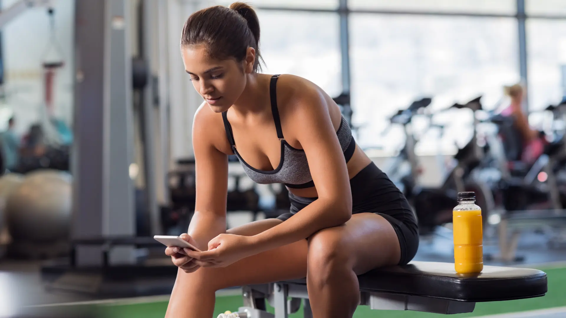 Frau trainiert im Fitnessstudio und nutzt eine Fitnessstudio-App auf dem Smartphone