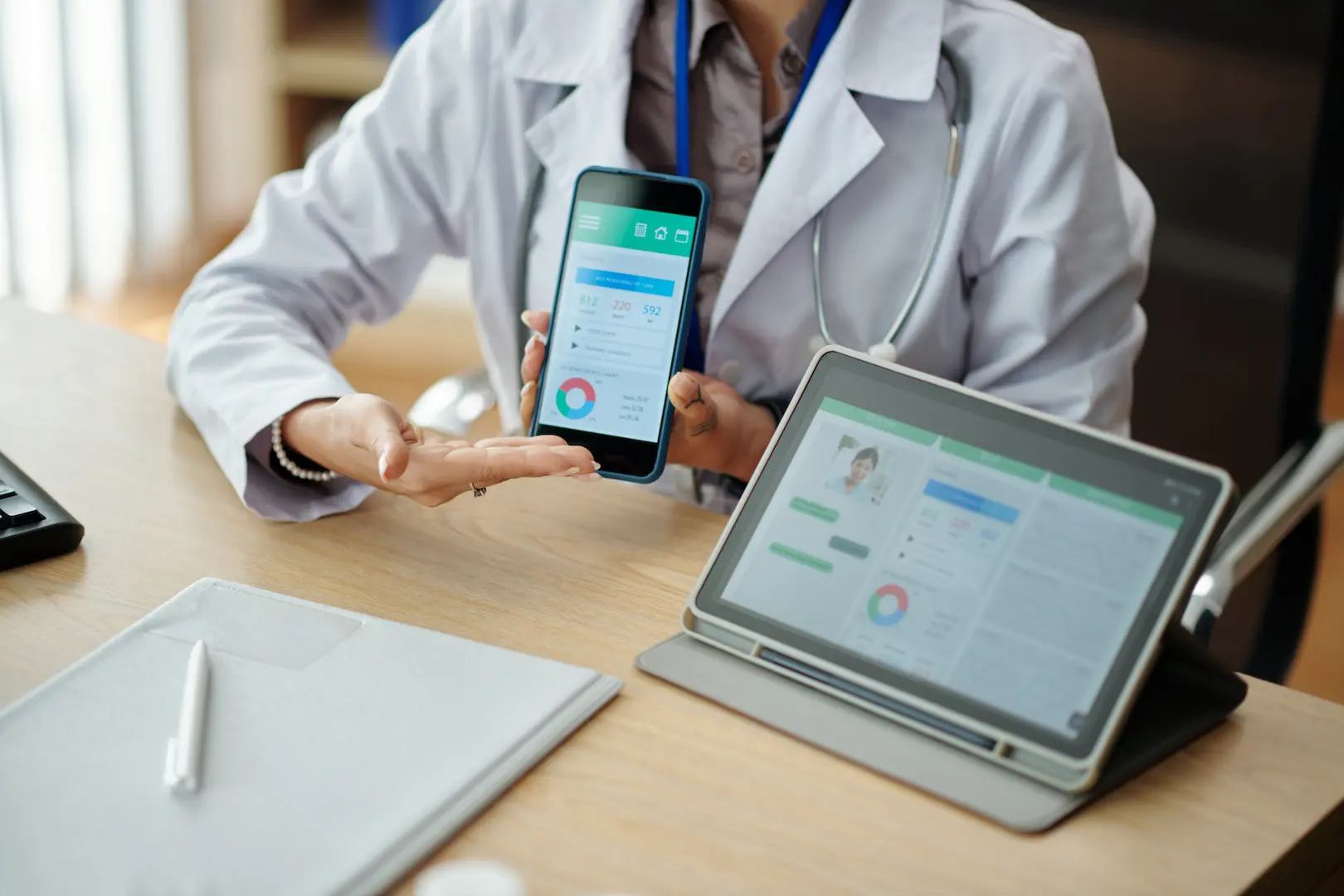 Ärztin zeigt einem Patienten eine Gesundheits-App mit Gerätedaten auf Smartphone und Tablet